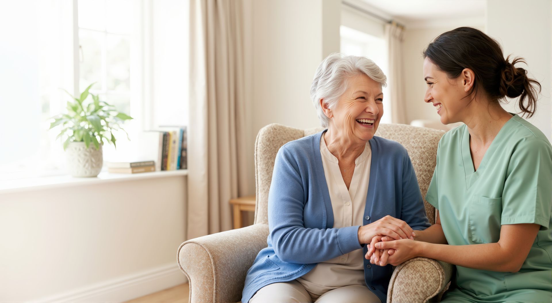 Two women smiling and holding hands on a couch in a bright living room