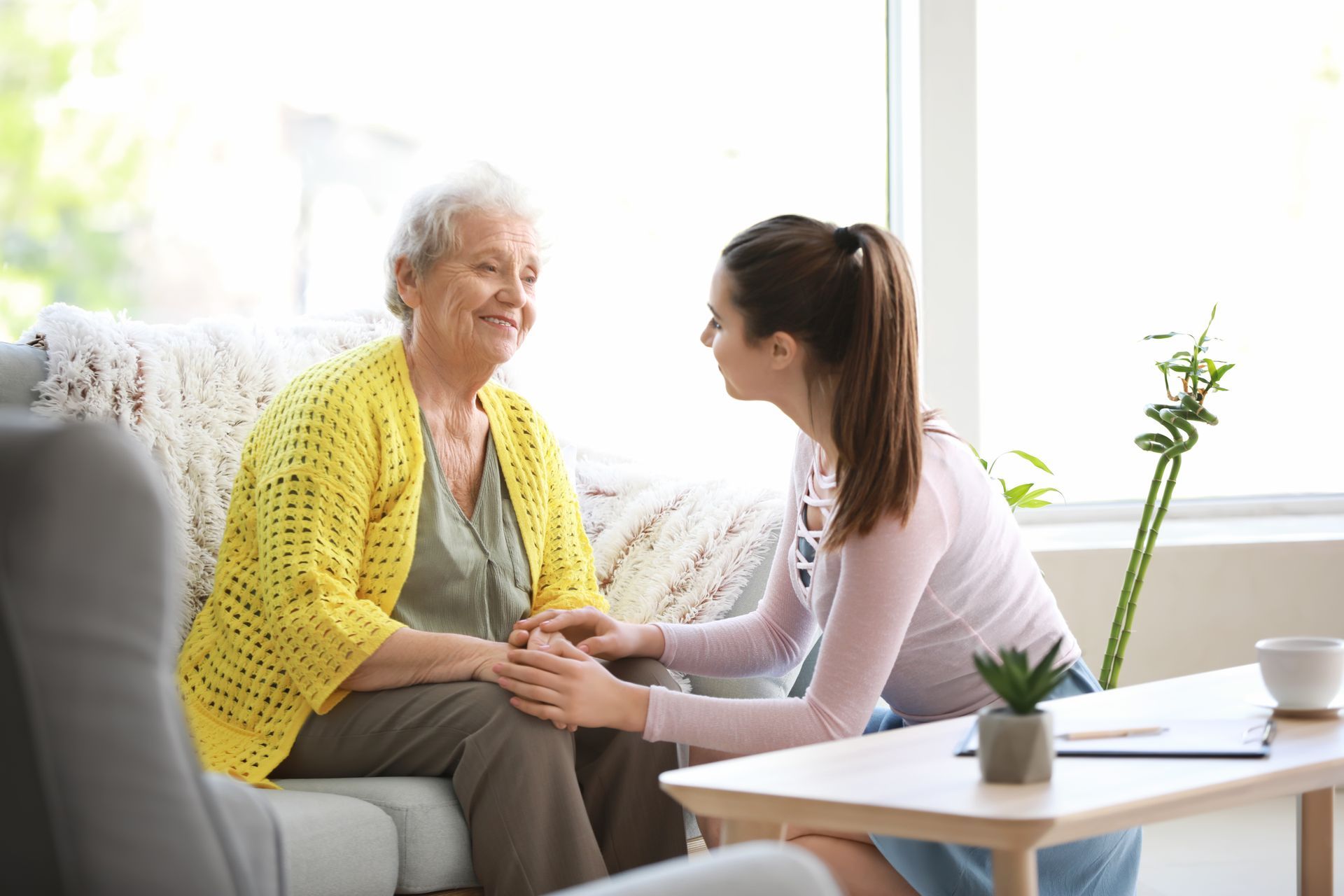Two women sitting and holding hands on a couch in a bright living room Two women sitting and holding hands on a couch in a bright living room
