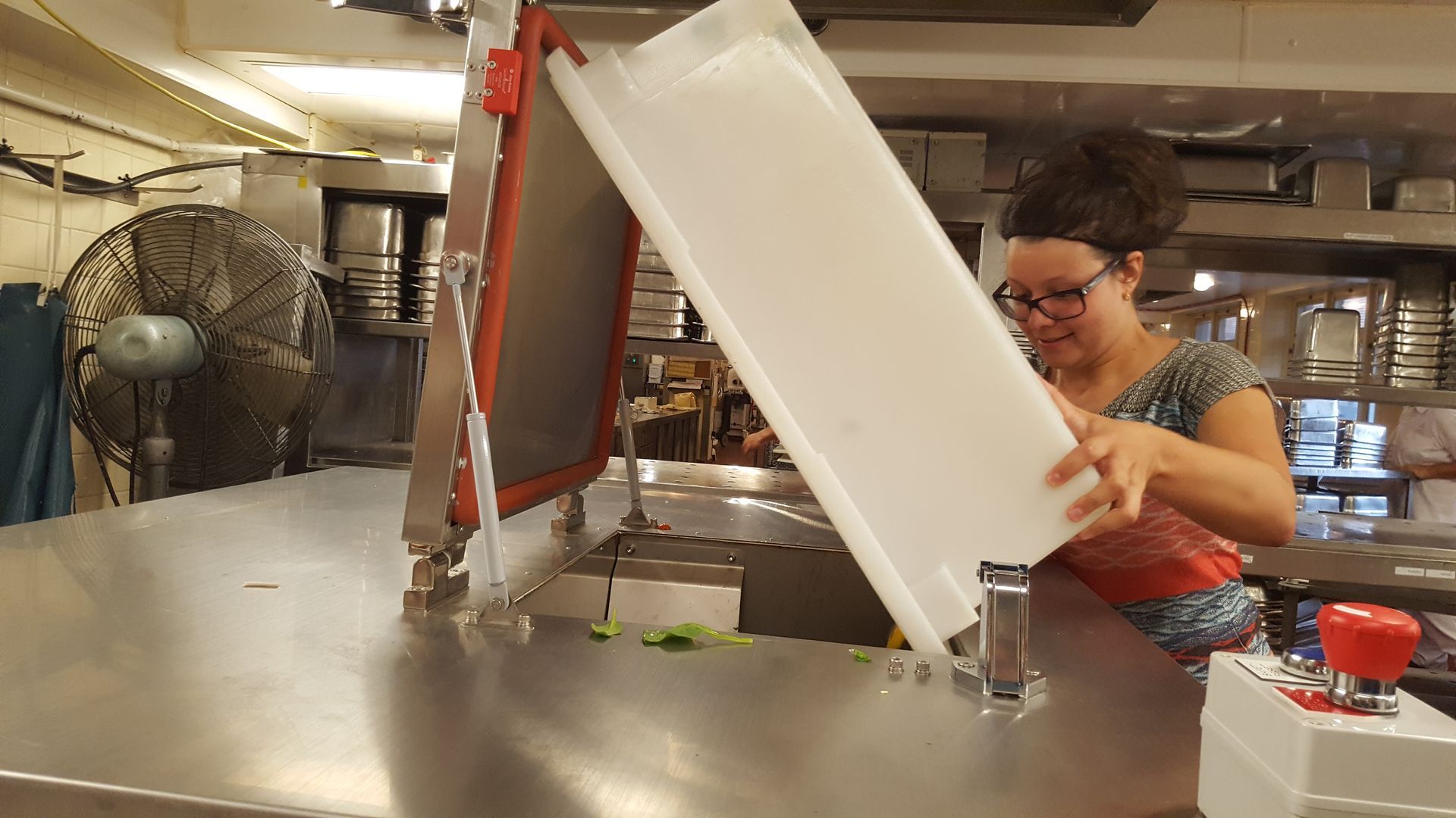 Une femme tient une poubelle blanche à côté d'une machine de sérigraphie dans une cuisine.