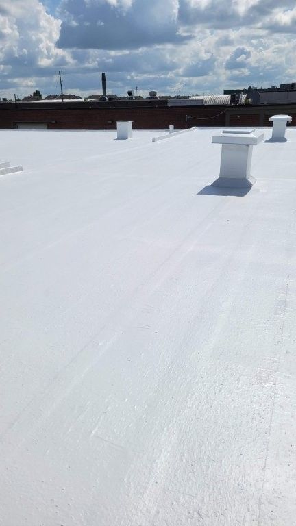 Toit plat blanc avec des conduits de ventilation sous un ciel partiellement nuageux.