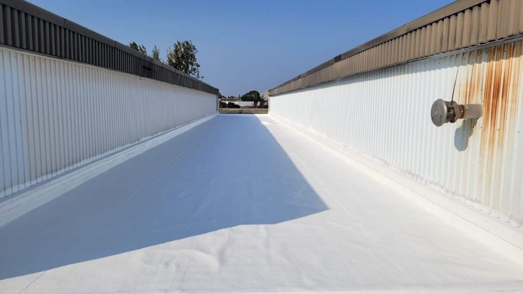 Vue depuis un toit industriel blanc, recouvert de bardage métallique des deux côtés, avec un tuyau rouillé et un ciel dégagé.