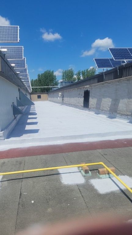 Un toit plat recouvert de panneaux solaires, revêtu d'un matériau réfléchissant blanc, sous un ciel bleu.