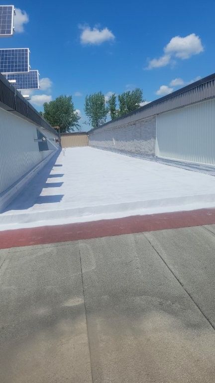 Toit plat blanc à rayure rouge, sous un ciel bleu parsemé de nuages ​​cotonneux.