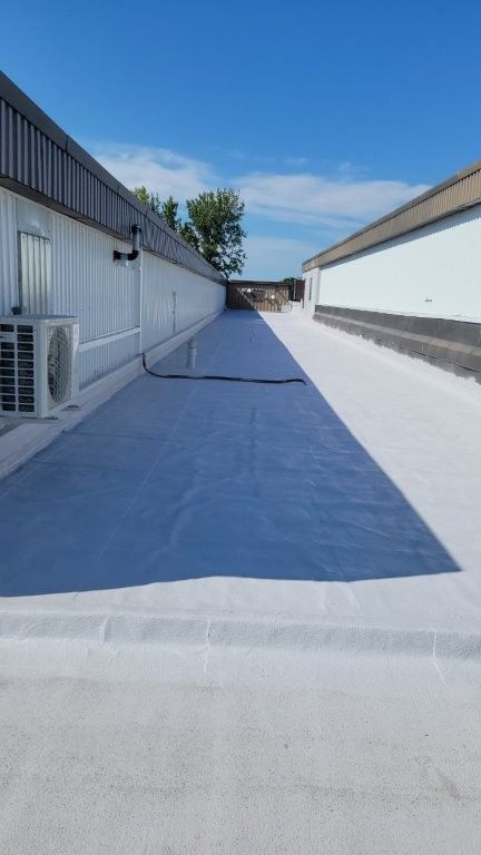 Toits commerciaux blancs avec une allée couverte d'une bâche bleue au soleil, bordée de bâtiments blancs sous un ciel bleu.