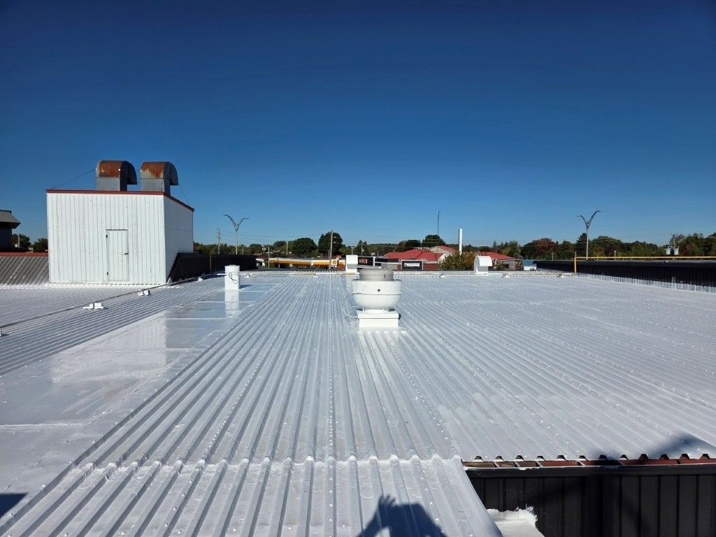Toit industriel blanc sous un ciel bleu limpide, avec des conduits d'aération et un petit bâtiment.