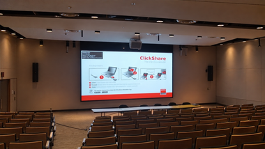 Empty auditorium with rows of seats facing a large projected presentation slide on the front screen