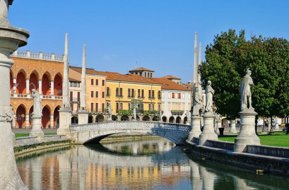 Prato della Valle a Padova, Italia, con statue, edifici e un cielo azzurro e limpido.