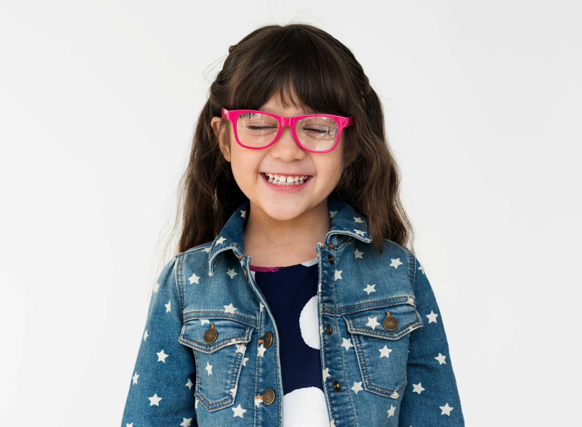 A little girl wearing glasses and a denim jacket is smiling.