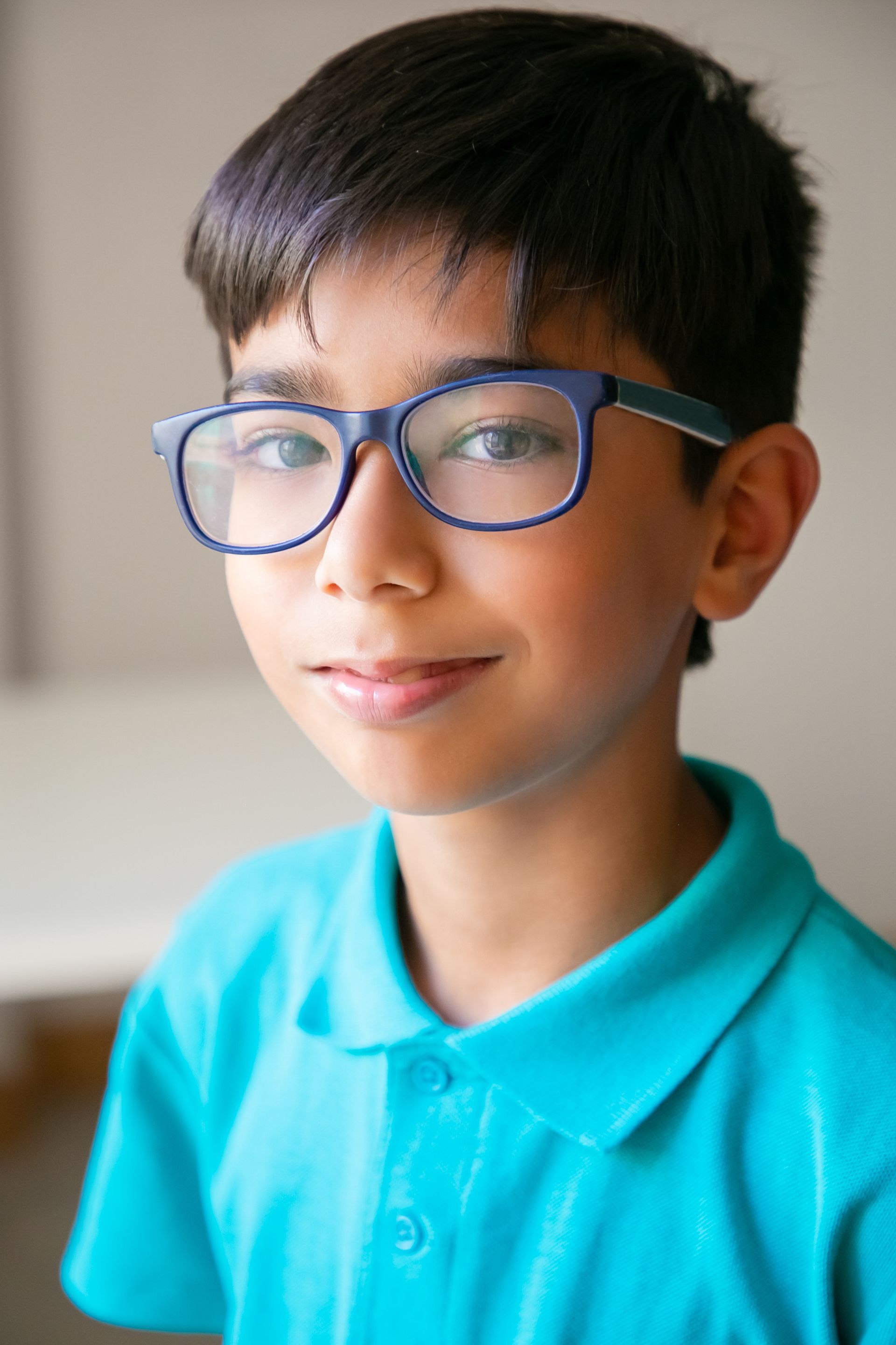 A young boy wearing glasses and a blue shirt is looking at the camera.
