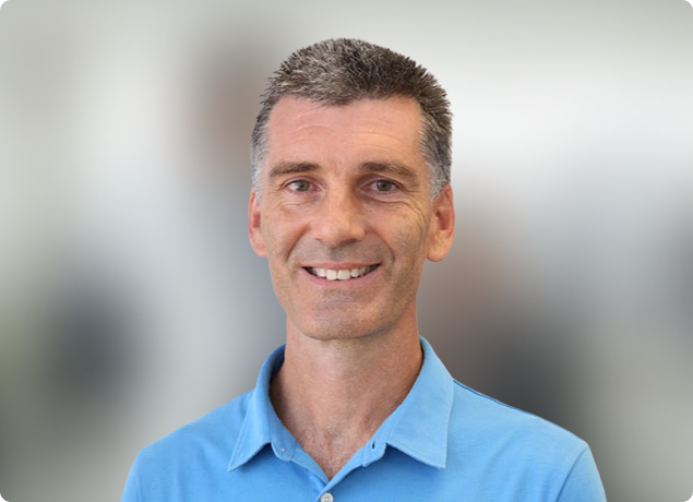 Smiling man in a blue polo shirt against a blurred indoor background