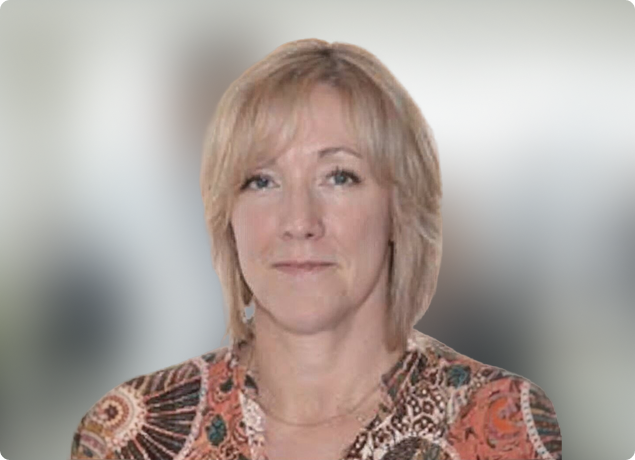Portrait of a blonde person in a patterned top, looking at the camera against a blurred background