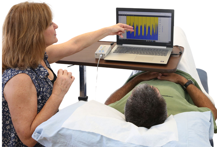 Therapist points to a monitor showing wave patterns while a patient lies on a treatment table