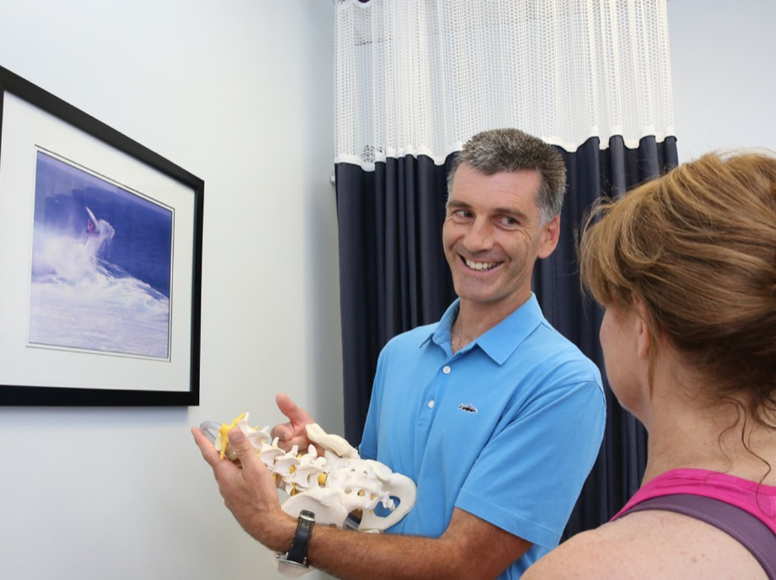 Man holding a bird skeleton model and smiling beside a framed bird photo on a wall