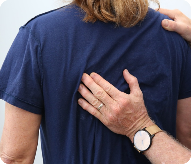 Hand on a person’s upper back during a comforting gesture, with a wristwatch visible.