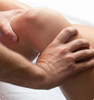 Hands massaging a bent leg on a white sheet