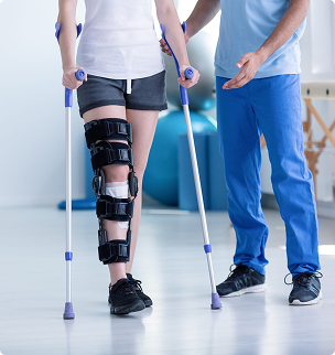 Person with knee brace using crutches, assisted by a physical therapist in a clinic