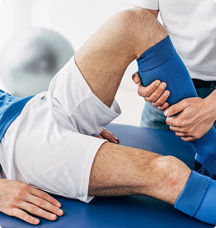 Physical therapist stretching a patient’s leg in a clinic, with blue support bandage and treatment table
