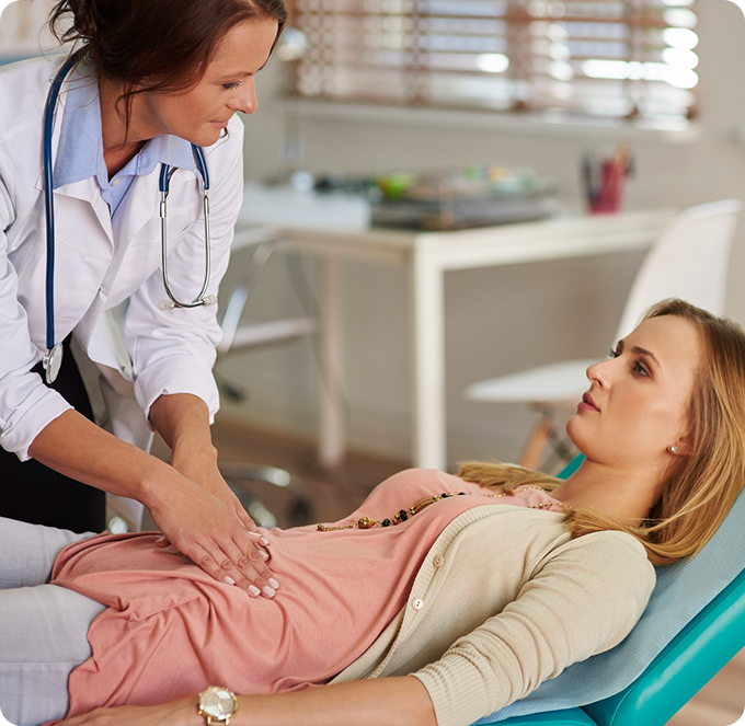Nurse checking a patient’s abdomen while she lies on an exam table in a clinic