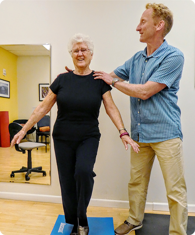 Two people practicing balance exercises in a studio, with one person supporting the other.