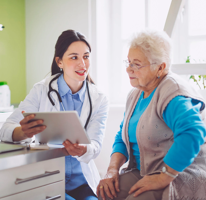 Doctor consulting with an elderly patient in a bright clinic, holding a tablet and smiling.