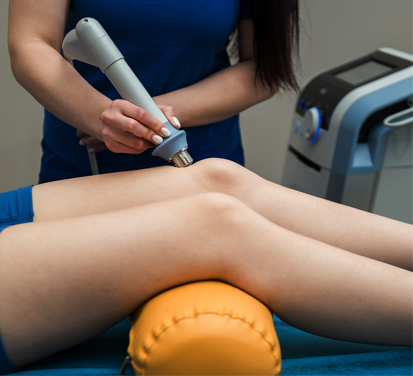 Legs resting on a cushion while a clinician uses a handheld device on the thigh in a treatment room