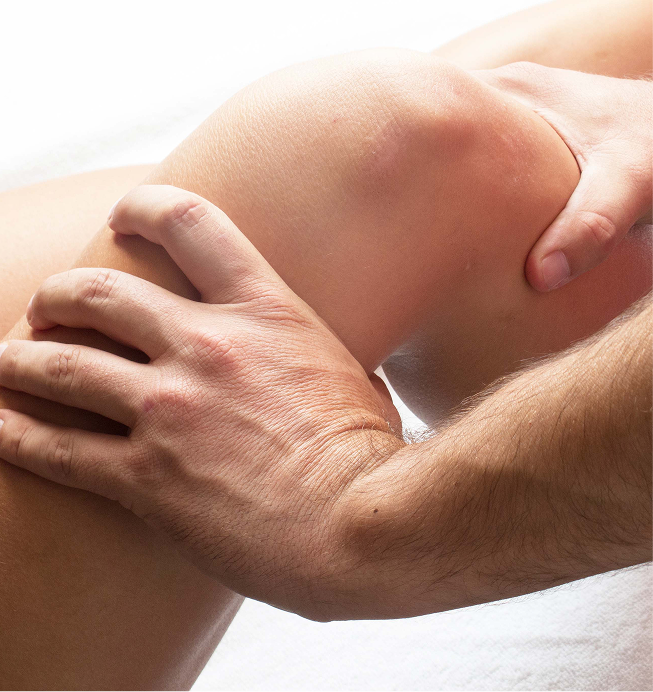 Close-up of hands massaging a bare knee or thigh in soft light