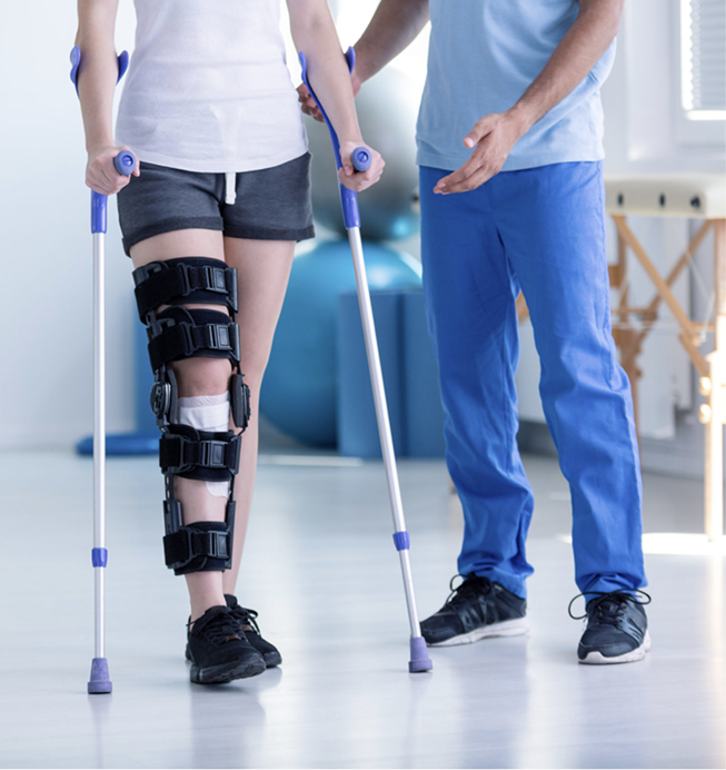 Physical therapist assisting a patient walking with crutches and a knee brace in a clinic