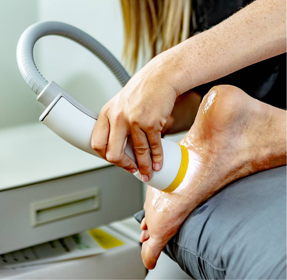 Person using a handheld device on a bare foot, likely for skin treatment or hair removal