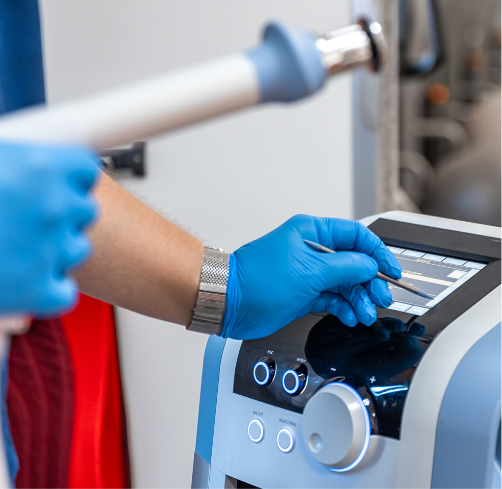 Gloved hands operate a medical device touchscreen beside tubing and control knobs