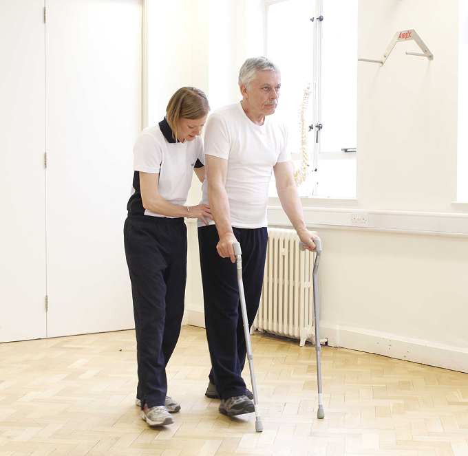 Caregiver helping a person walk with a cane in a bright room with wooden floors