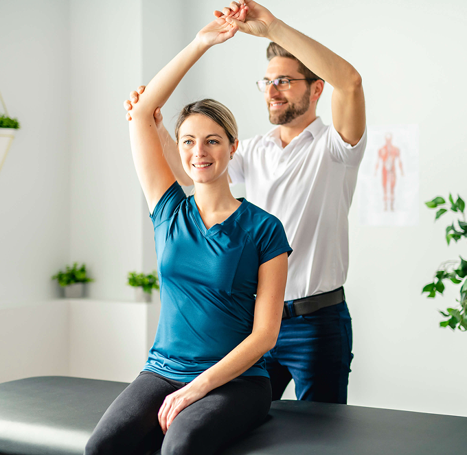 Physical therapist guiding a smiling patient in seated arm stretch on a treatment table