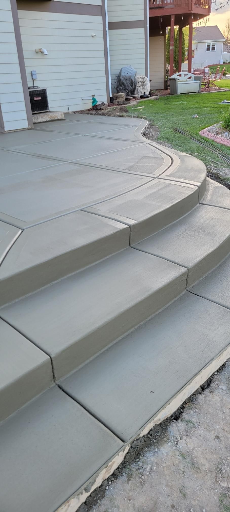 Curved concrete front steps and sidewalk leading to a house entrance, with a small garden nearby