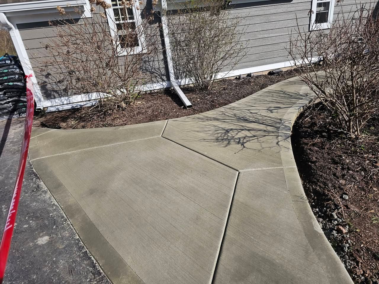 Concrete sidewalk with a large crack beside a house and landscaping, marked by a red line on the left