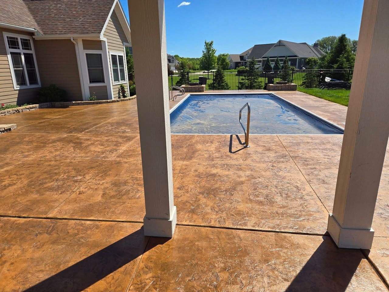 Backyard stamped concrete patio installed around swimming pool, white columns, and a house in the background