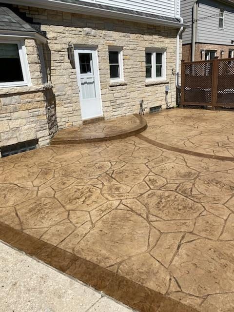 Stamped concrete patio beside a stone house, with a white door and curved step.