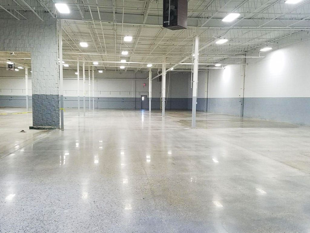 Empty large warehouse with polished concrete floor, white columns, and overhead lights
