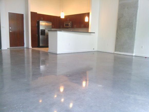 Empty modern apartment living area with polished concrete gray floor and a small kitchen/bar in the background