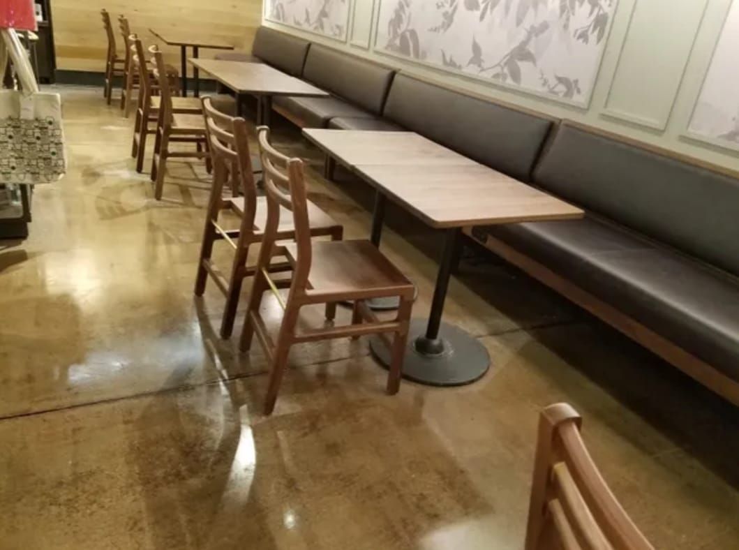 Polished concrete in empty café seating area with wooden chairs, long tables, and a cushioned bench along the wall.