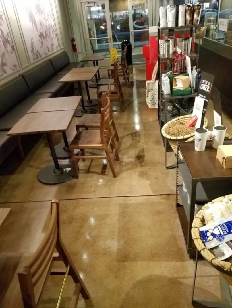 Polished concrete in empty café with wooden tables and chairs, counter items, and a glass entrance in the background
