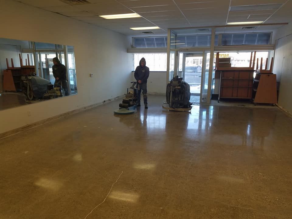 Person polishing concrete in empty room with a floor buffer near large windows and mirrors