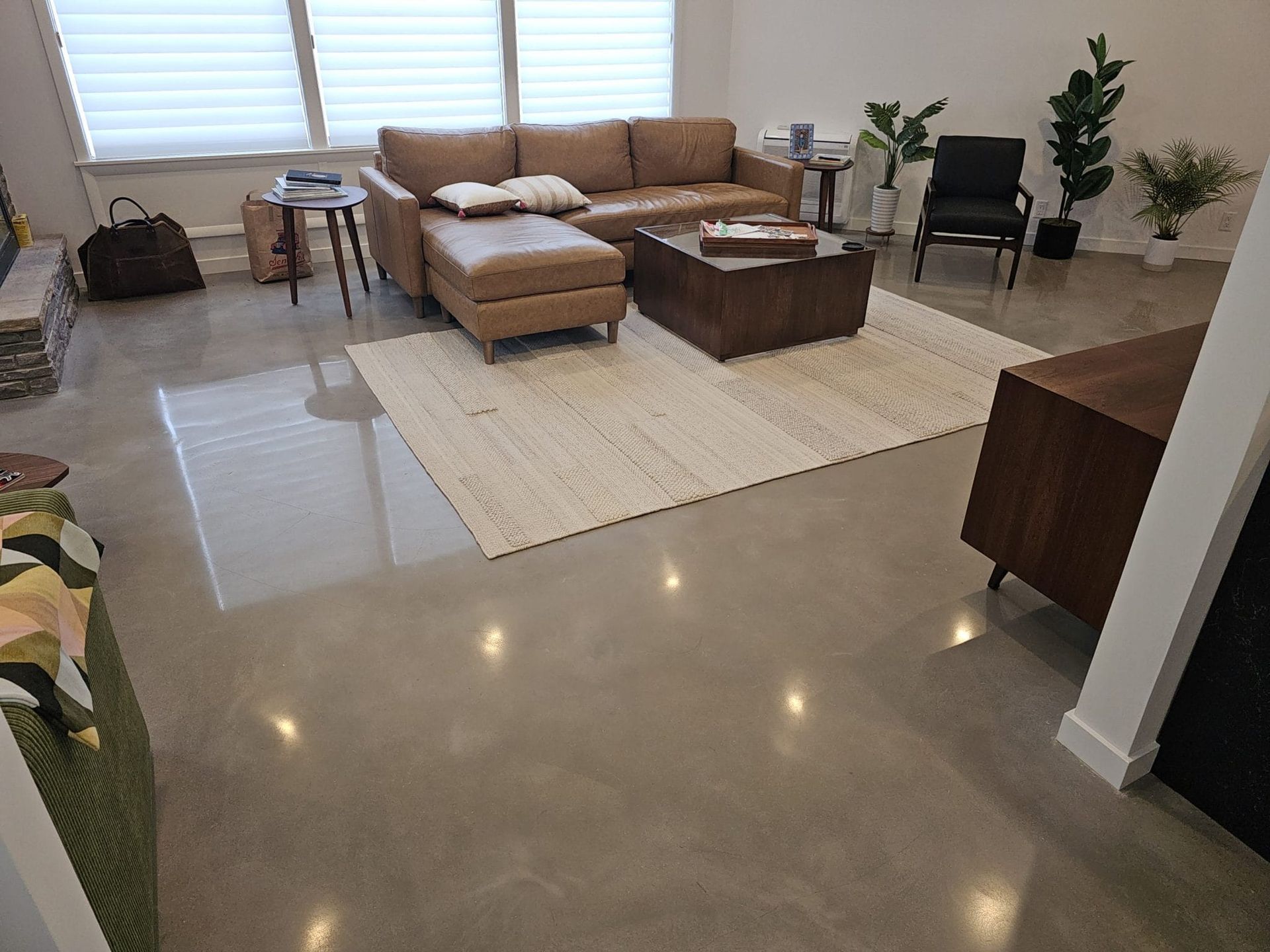 Modern living room with tan sectional, ottoman, rug, coffee table, and polished concrete tiles by windows.