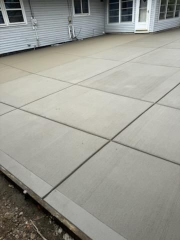 Concrete backyard patio beside a house, with light gray slabs and expansion joints.