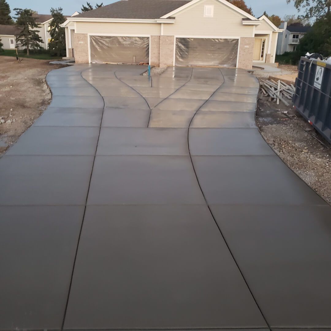 Freshly poured concrete driveway leading to a garage, with plastic sheeting over the new slabs.