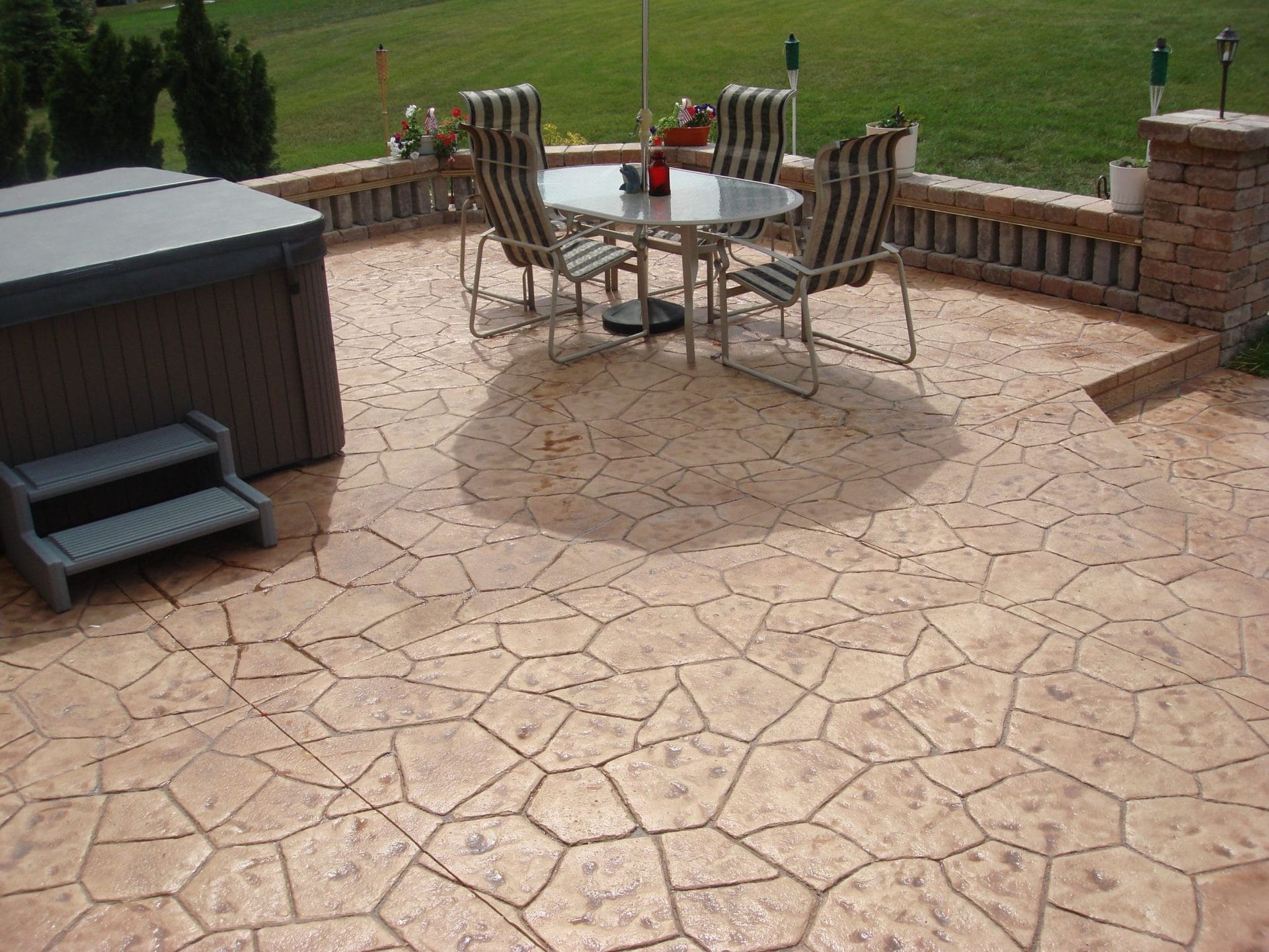 Patio with stamped concrete, metal table and chairs, hot tub, and grassy yard beyond