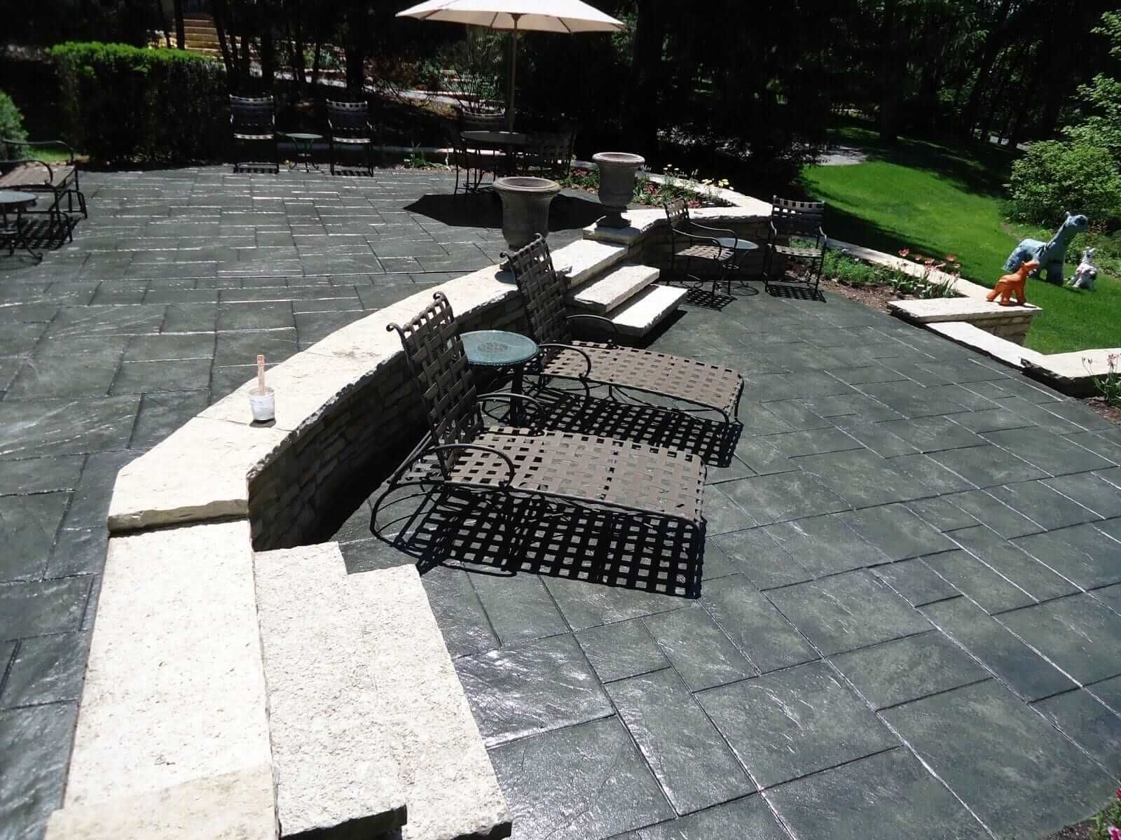 Stamped concrete patio with built-in seating, black pavers, and a sunlit backyard lawn