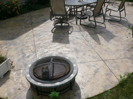 Stamped concrete patio with stone pavers, metal chairs, and a circular fire pit in the foreground