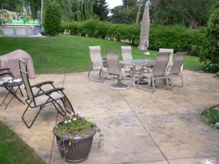 Stamped concrete patio with metal chairs and table beside a green lawn and garden shrubs