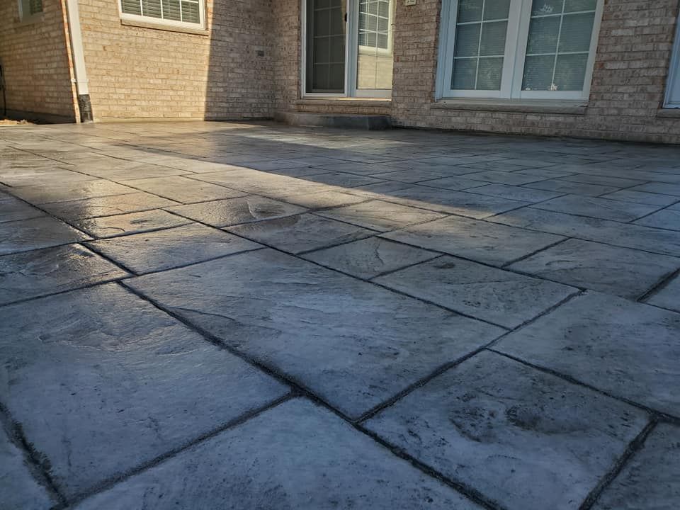 Stamped concrete patio in front of a brick house with windows and sunlight casting shadows