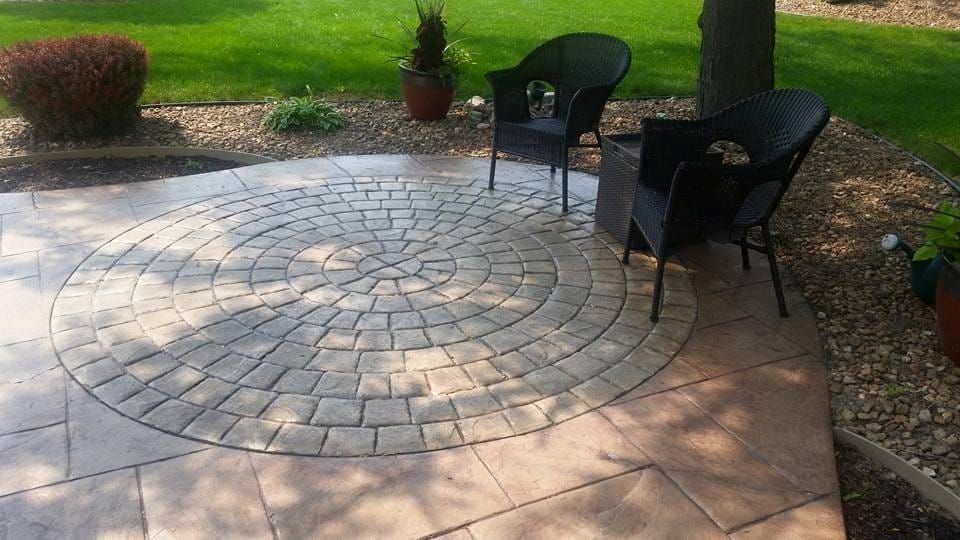 Circular stamped concrete patio with two black chairs and a small table in a landscaped garden