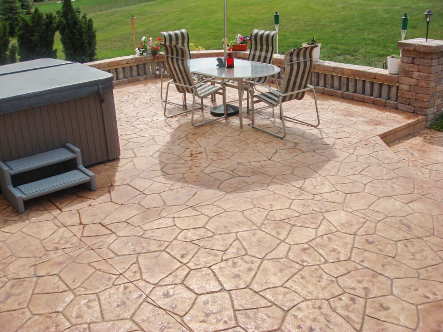 Stamped concrete patio with outdoor dining table, chairs, grill, and countryside view.